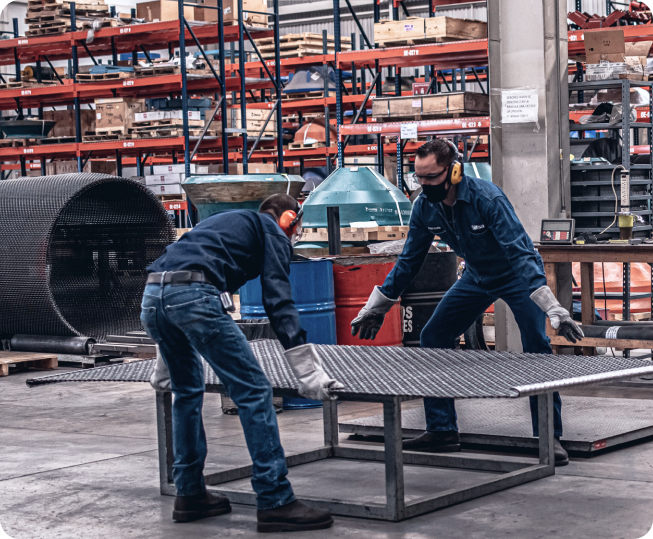 Dos trabajadores en un taller manipulando una malla de criba